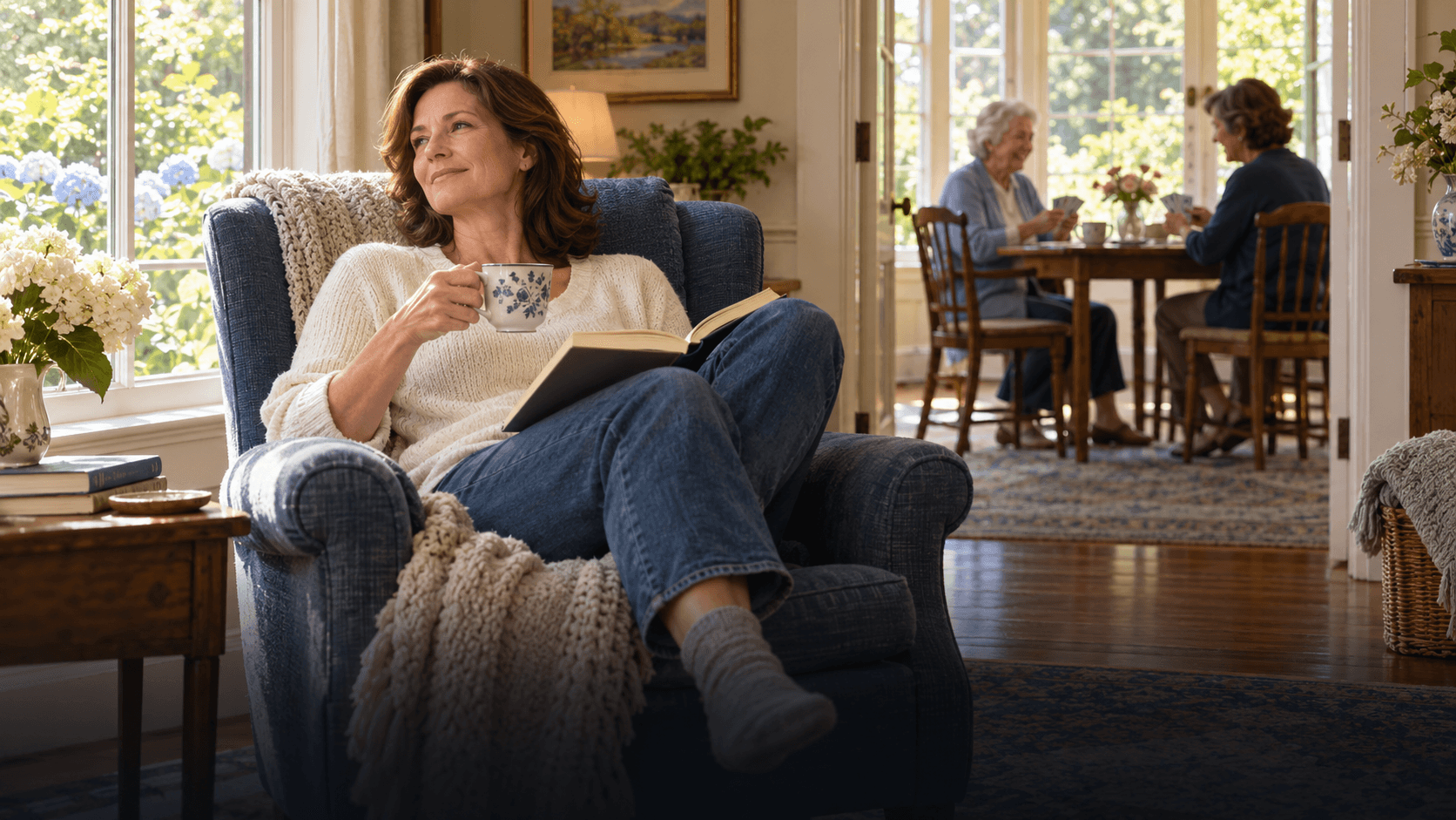 Family caregiver resting with tea and a book while a companion visits with an older adult